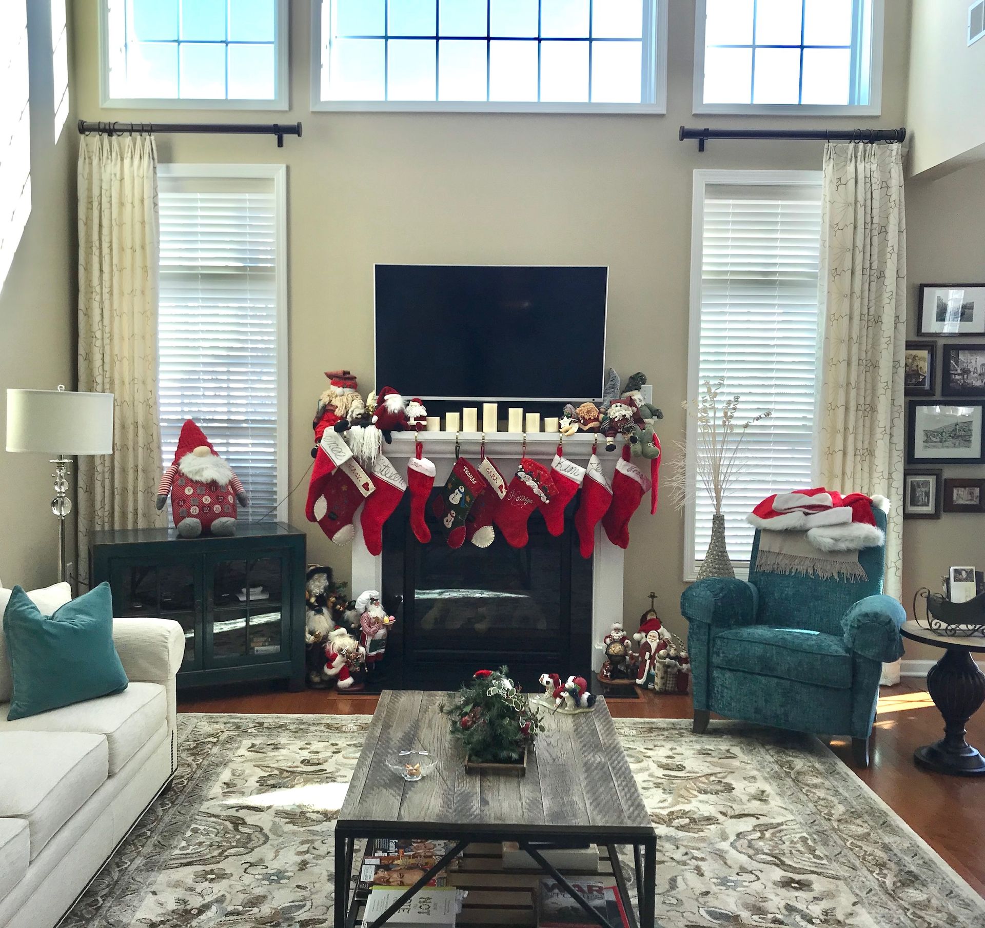 Living room with Christmas decorations: fireplace with stockings, Santa, tree, couch, armchair, window.