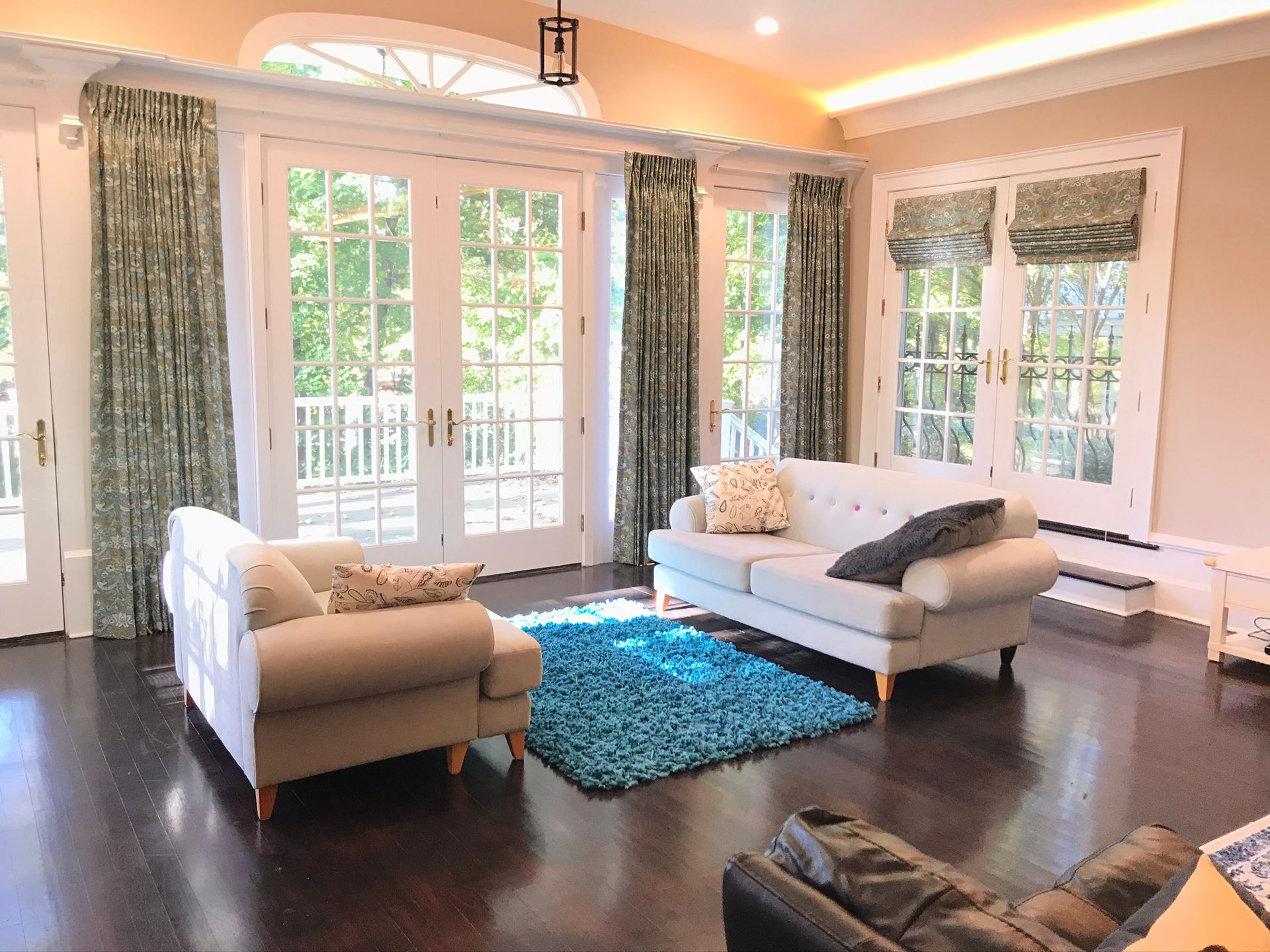 Living room with French doors, tan walls, blue rug, two sofas, and patterned curtains.