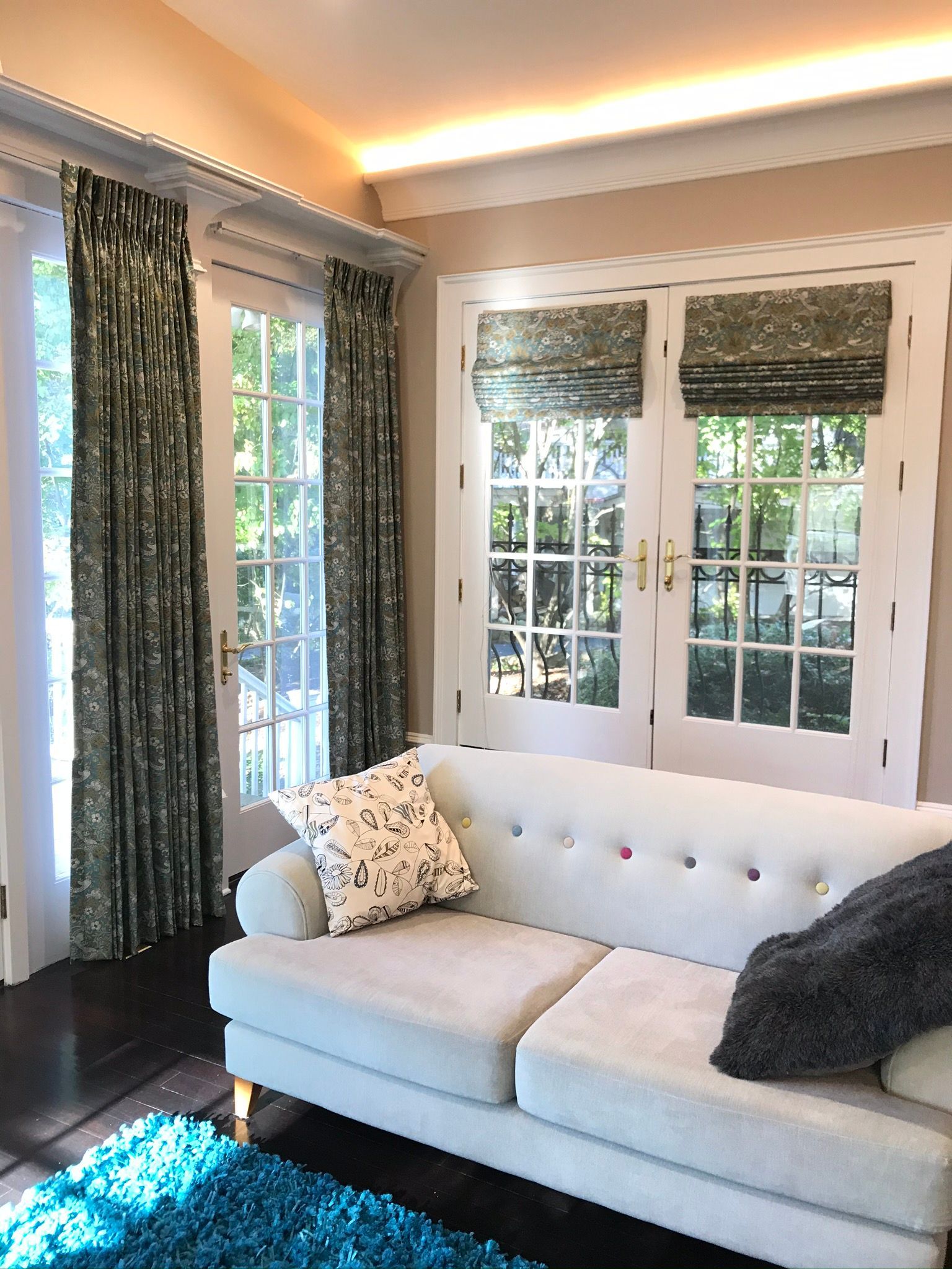 A living room with French doors and a light blue sofa, curtains, and a teal rug.