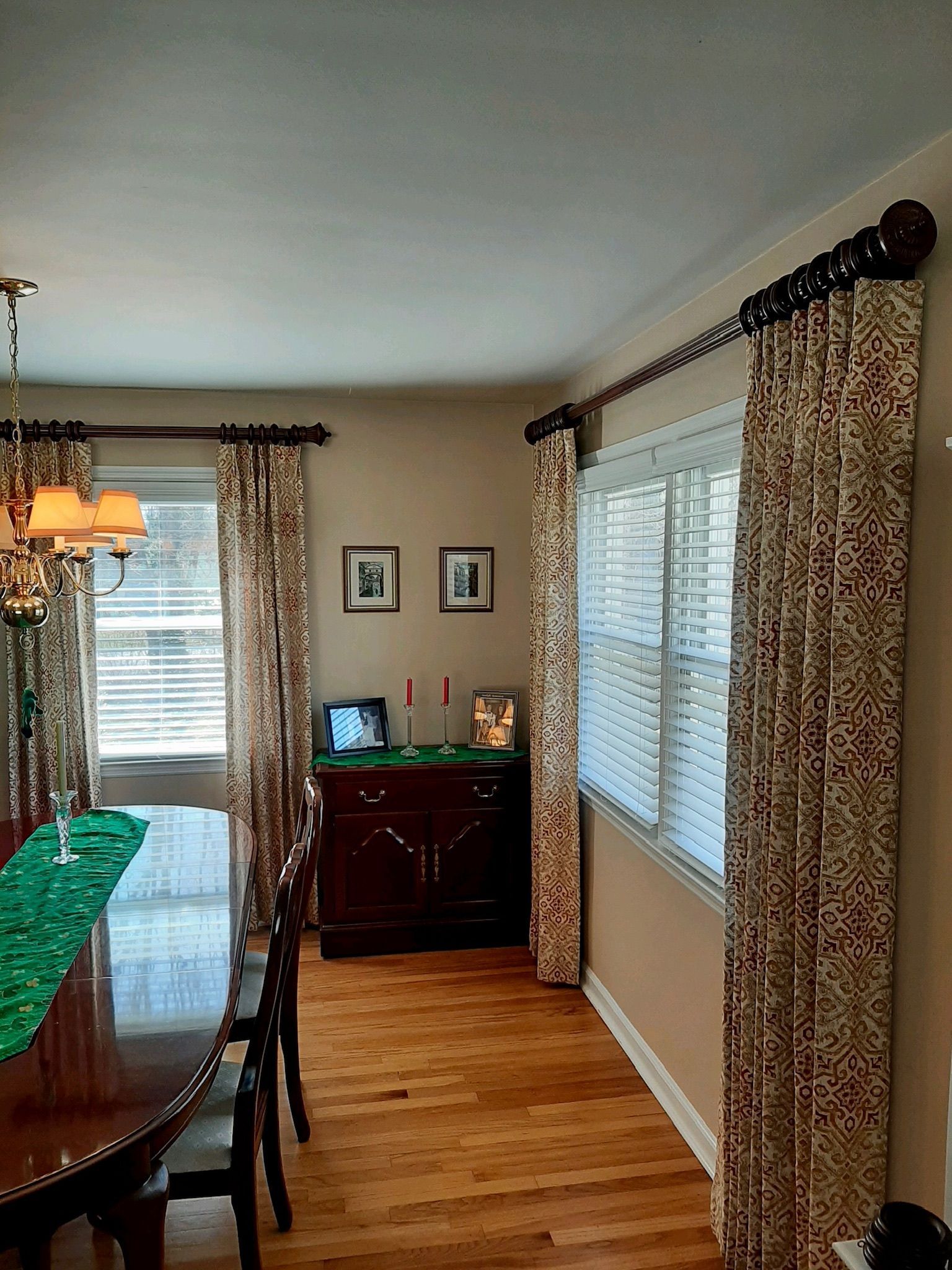 Dining room with patterned curtains, wooden table, buffet, hardwood floor, and chandelier.