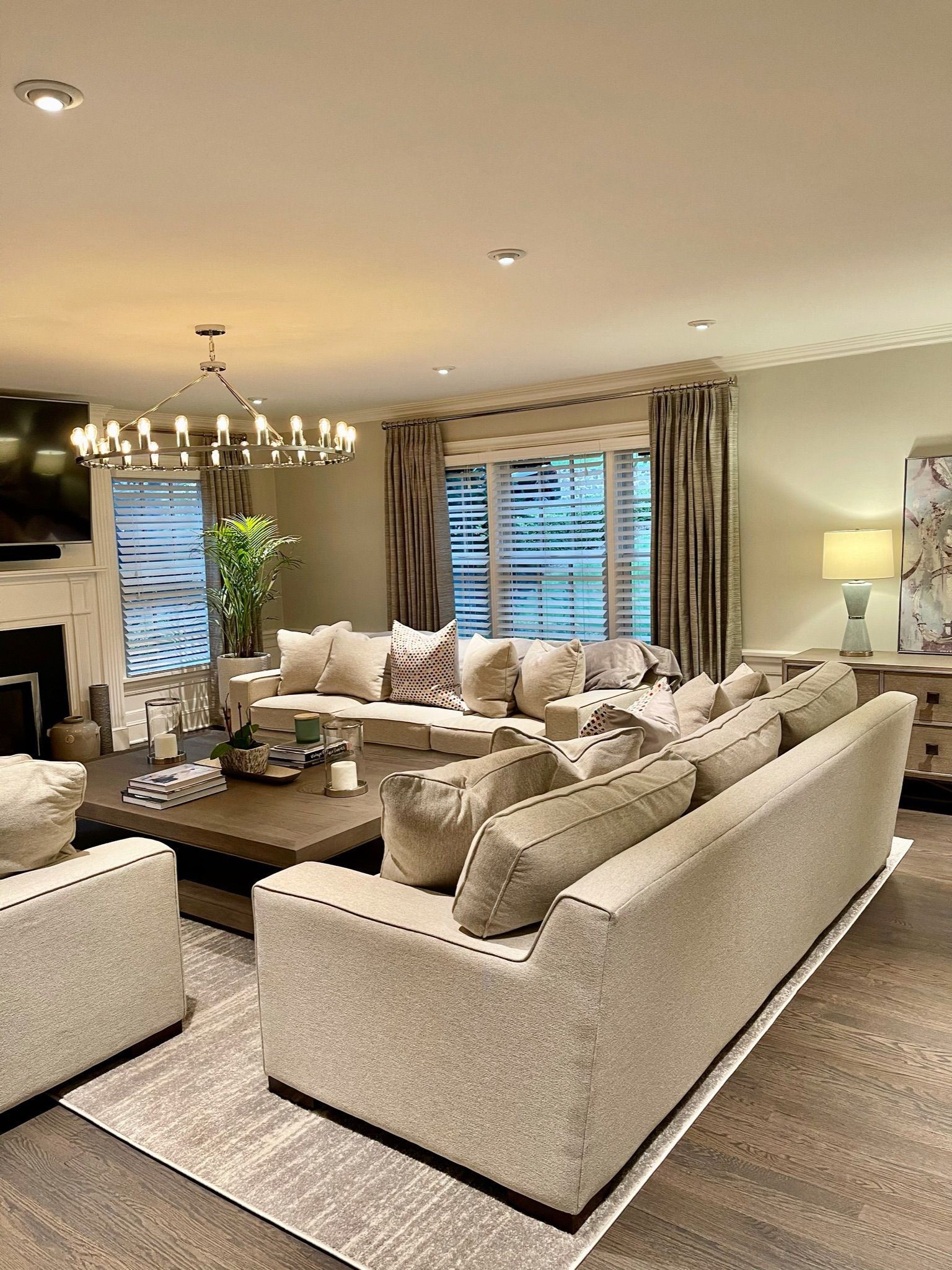Living room with beige sofas, patterned rug, and window with blinds and curtains.