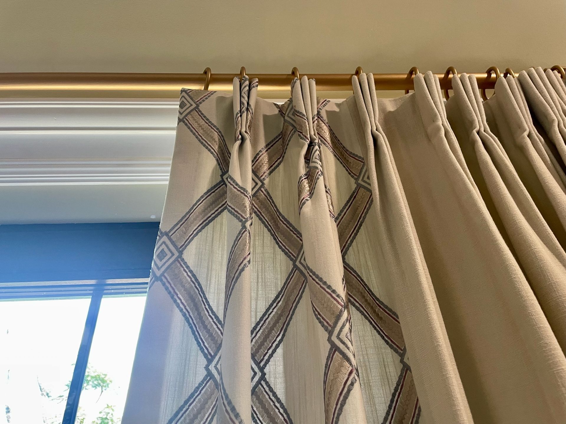 Beige curtains with a diamond pattern hanging from a gold rod above a window.