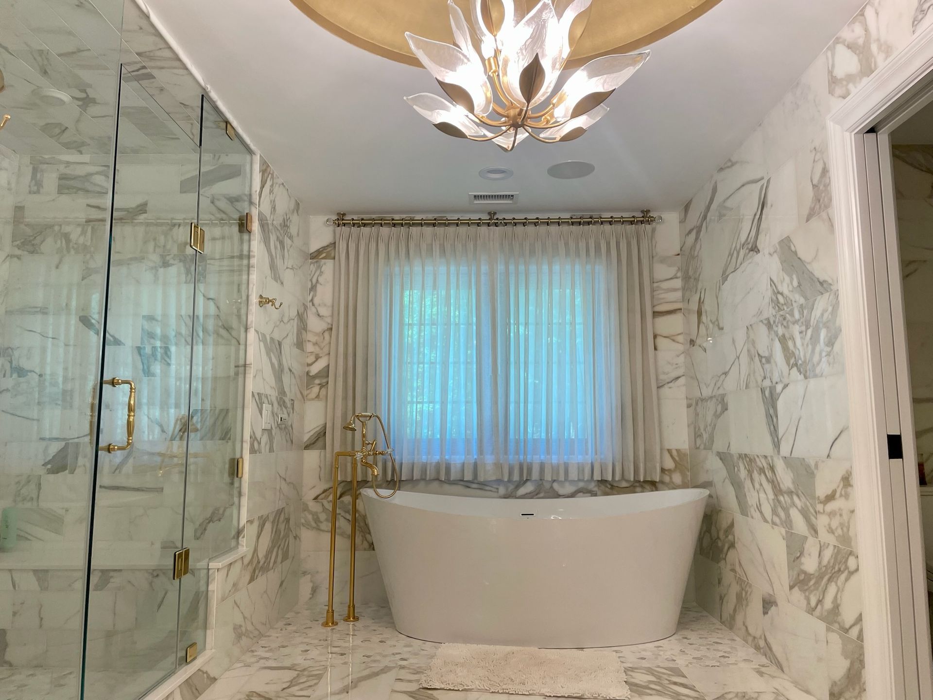 Luxurious bathroom with white marble walls, a freestanding tub, and an ornate chandelier.
