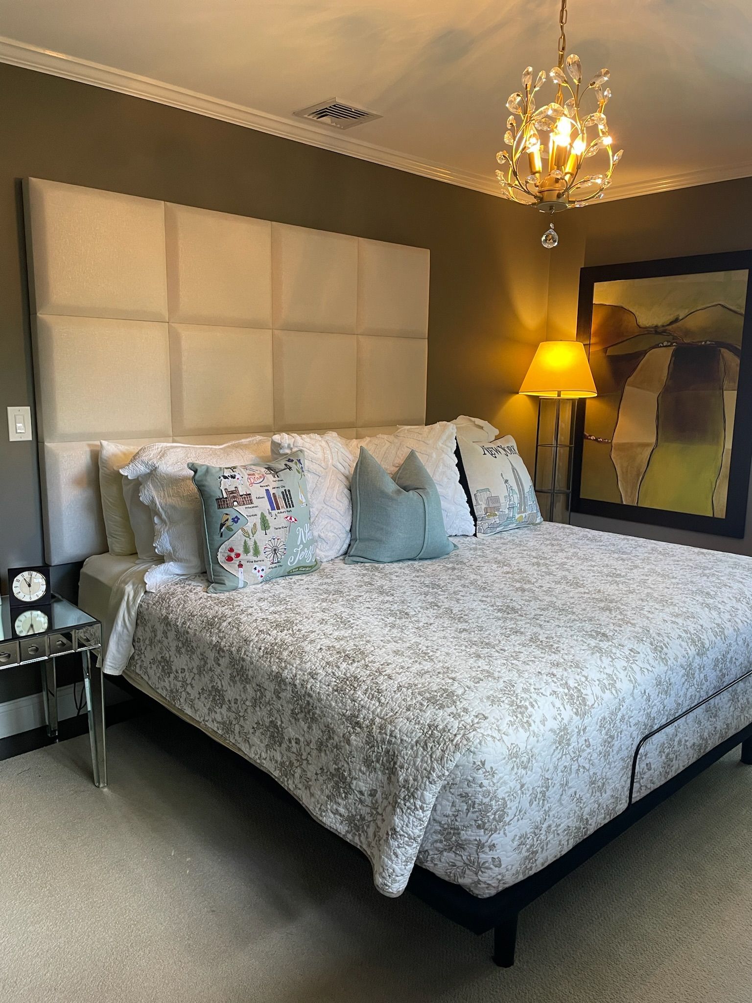 Bedroom with a large bed, upholstered headboard, and decorative pillows. A chandelier and abstract art are also present.