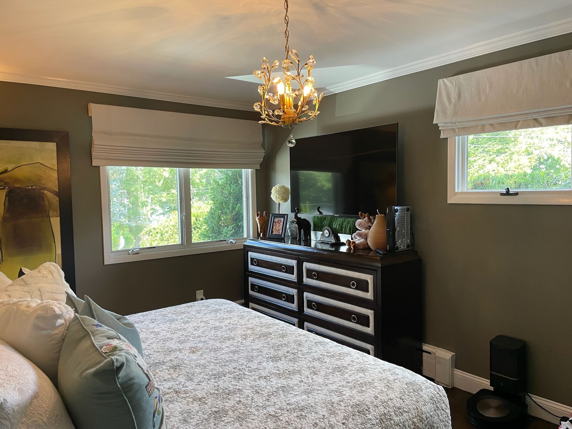 Bedroom with bed, dresser, TV, window, gold chandelier; neutral colors.