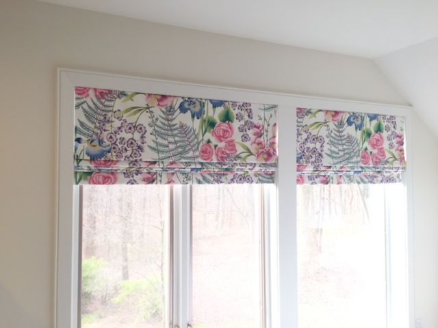 Floral Roman shades cover a window, framed in white, inside a cream-colored room.