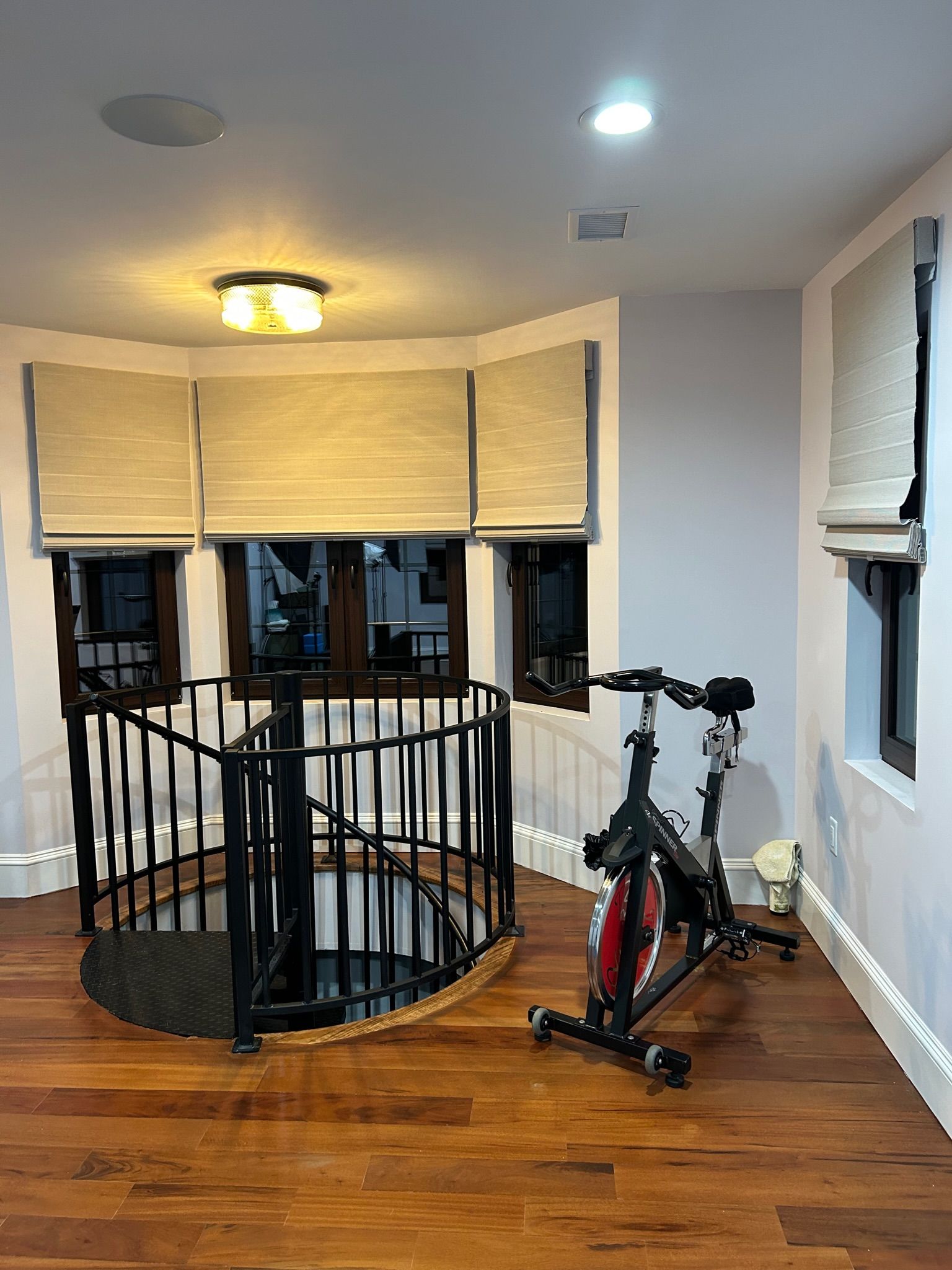 A home gym with a spiral staircase, exercise bike, and windows with blinds.