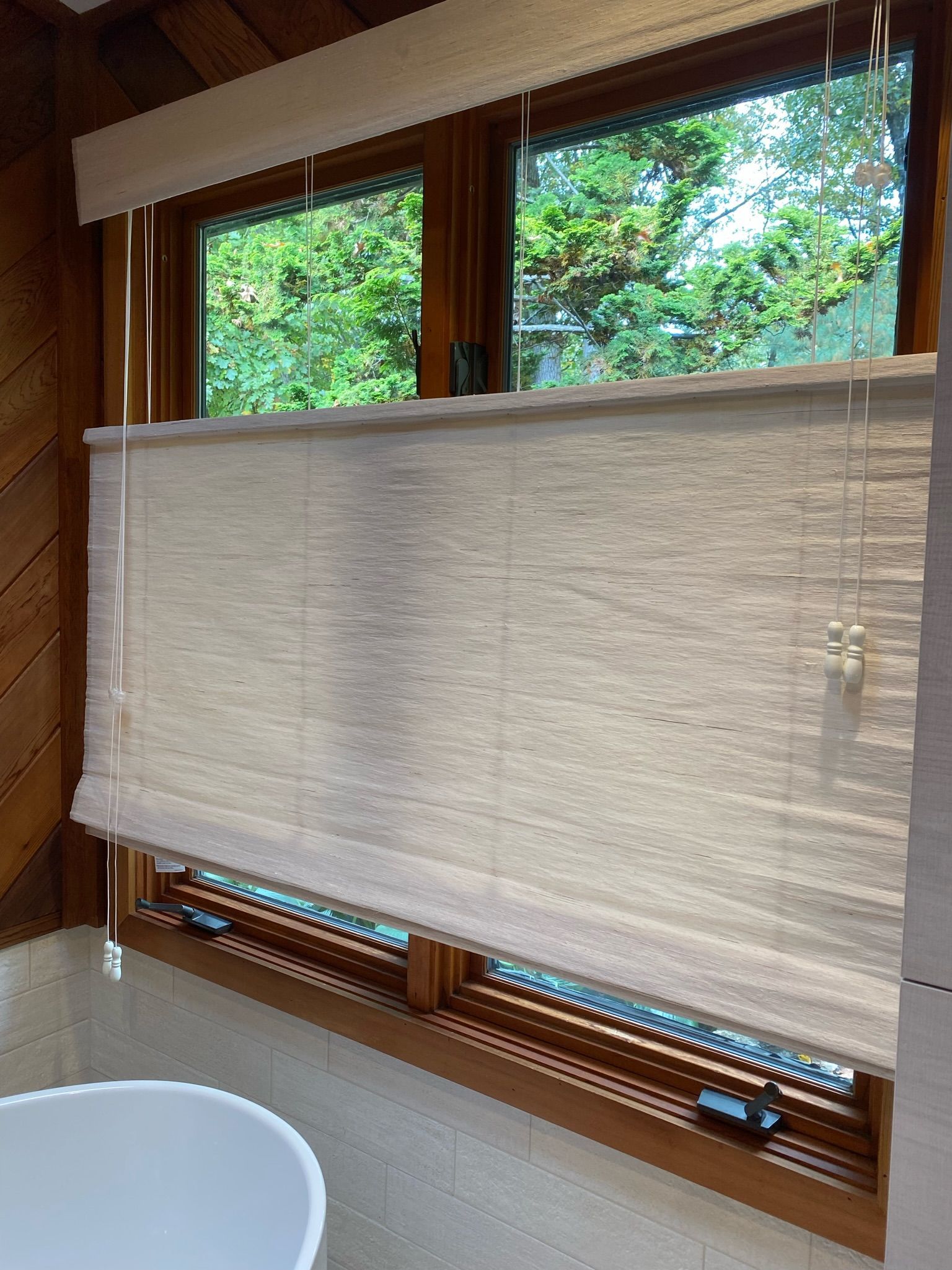 Close-up of a window with natural woven shades, overlooking green foliage. Wooden window frame.