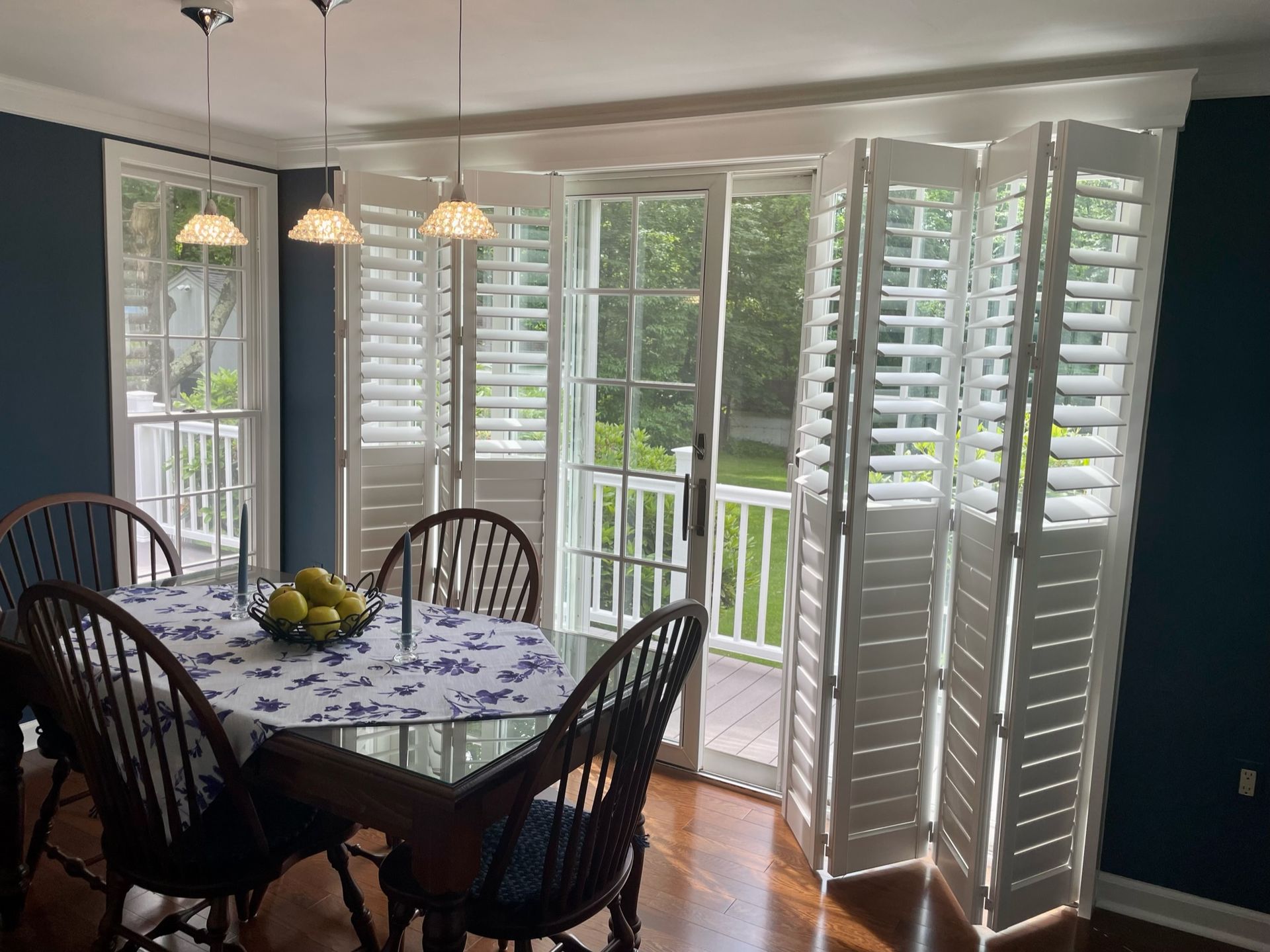 Dining room with table, chairs, shutters, and sliding glass doors overlooking a porch and yard.