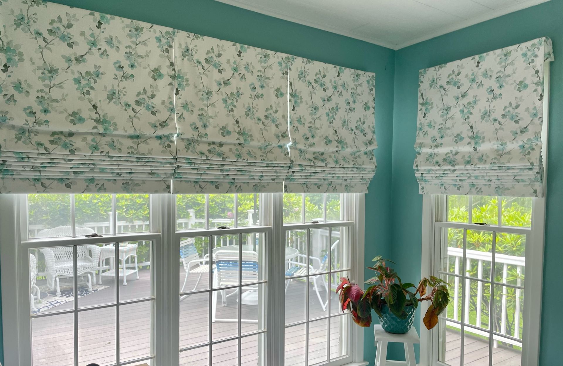Roman shades with floral pattern on windows in a turquoise room with white trim.