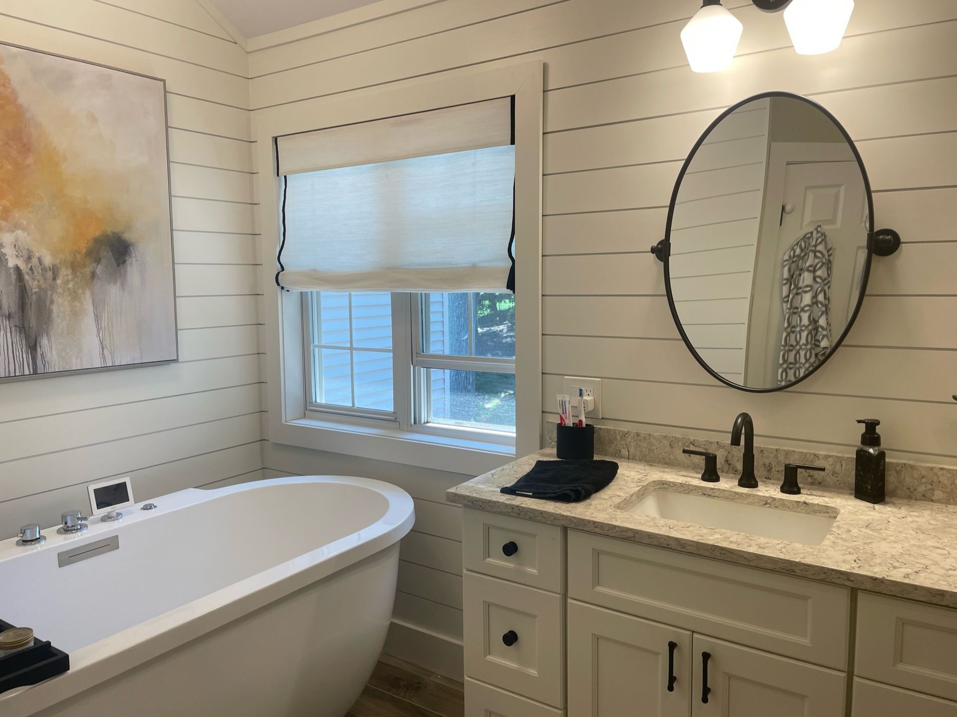 Bathroom with white tub, vanity, window, mirror, and abstract painting.