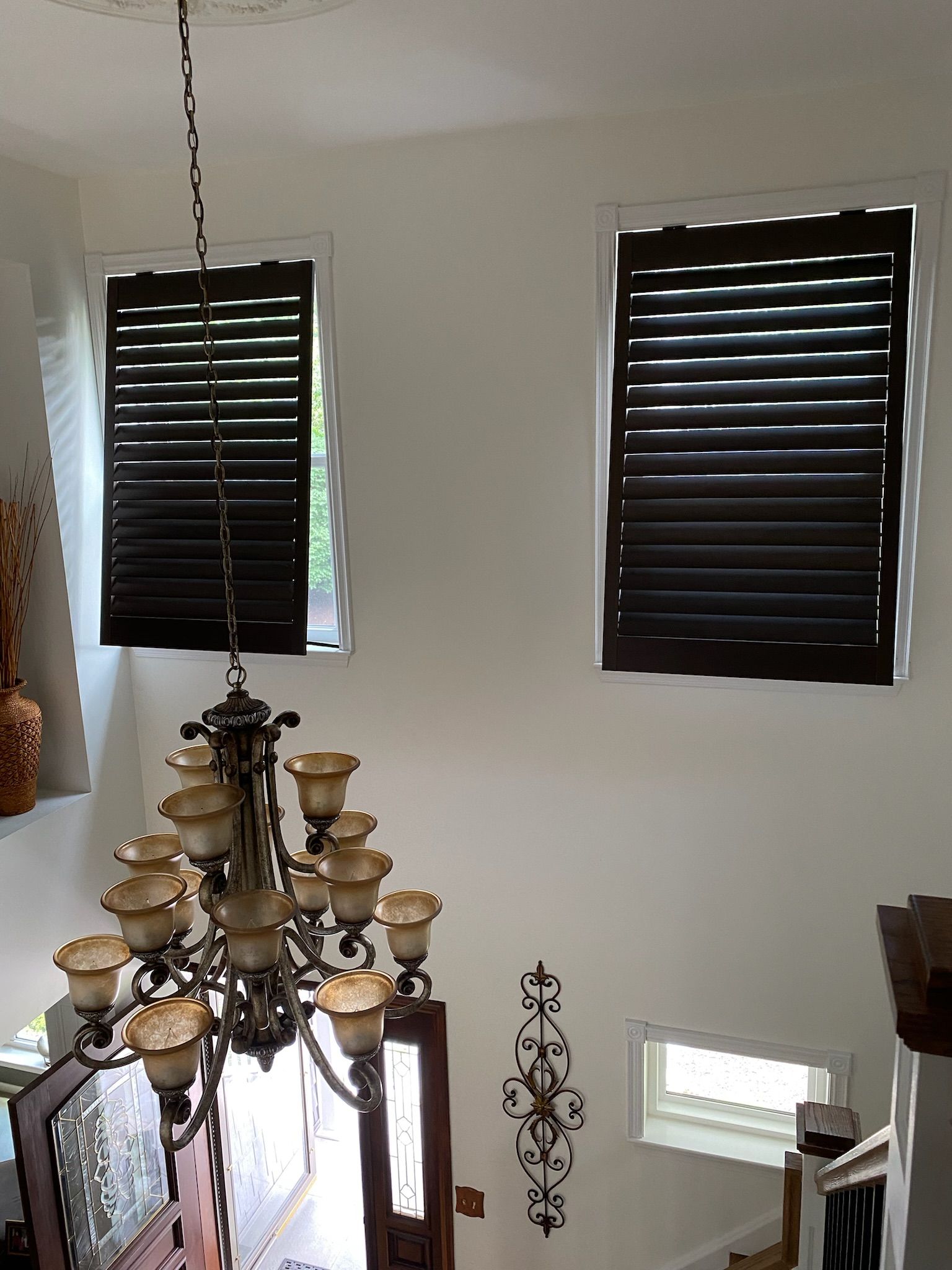 Two windows with dark brown shutters, a chandelier, and a stairwell.