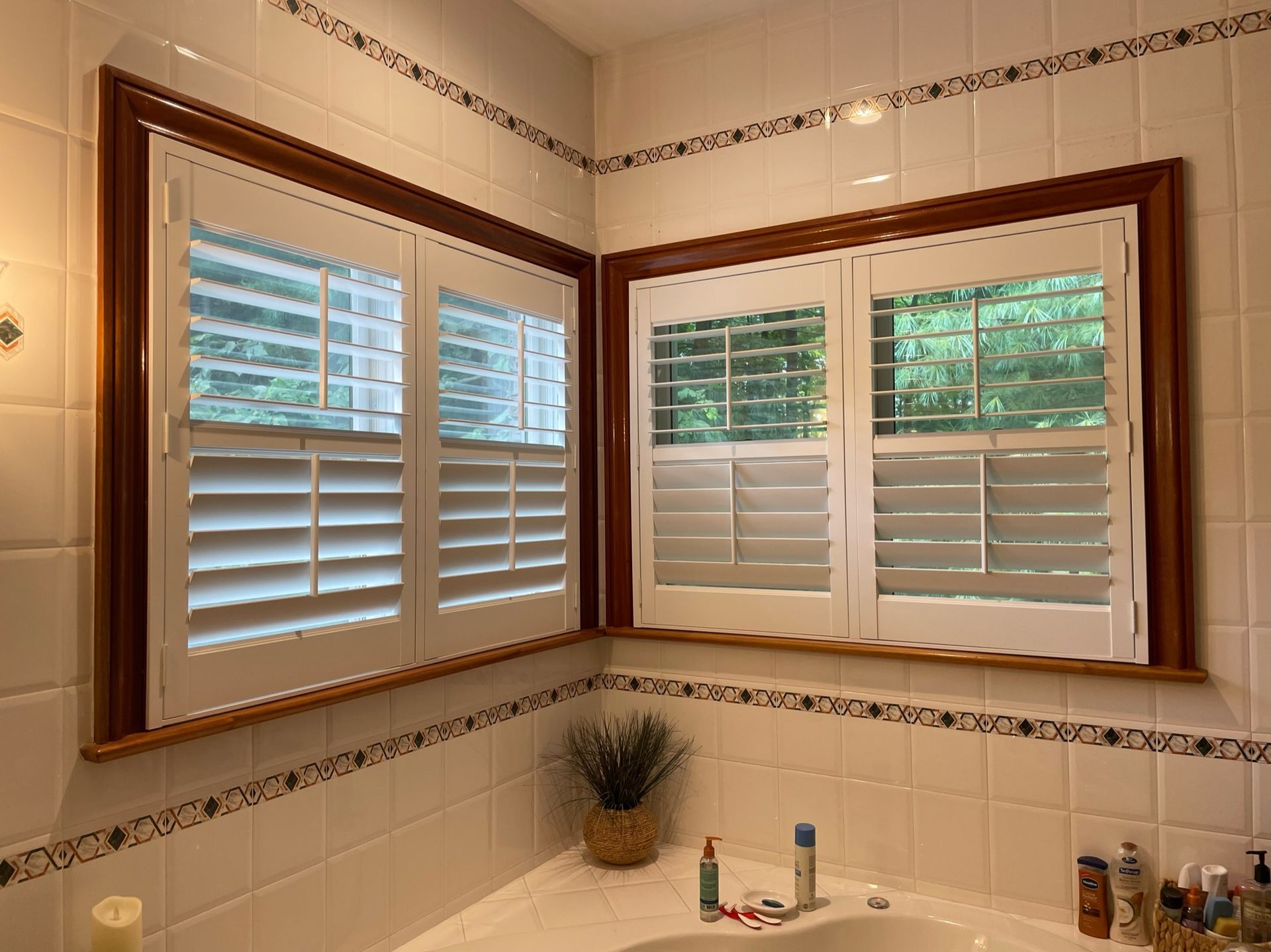 Bathroom with white tile, a corner window with white shutters and brown trim.