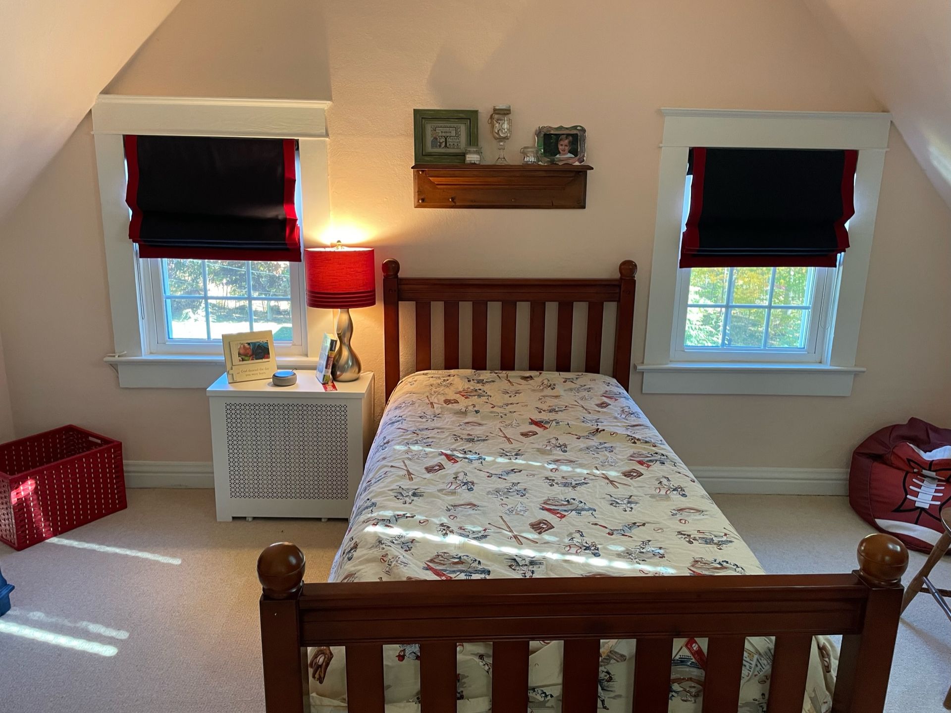 Bedroom with a wooden bed, two windows with black shades, a bedside table, and a red lamp.