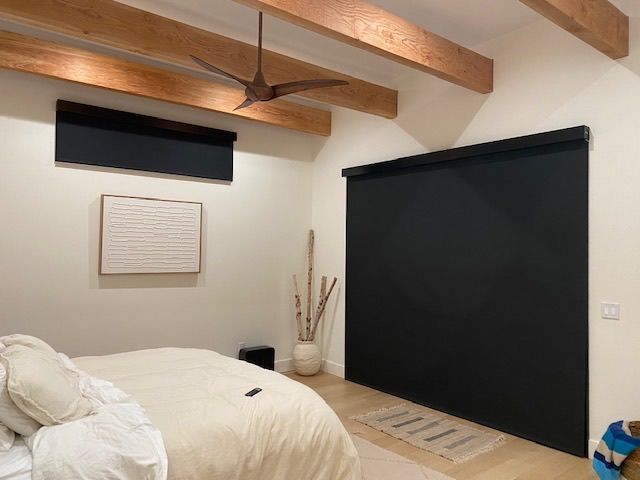 Bedroom with black blinds, wooden beams, white walls, and a bed.