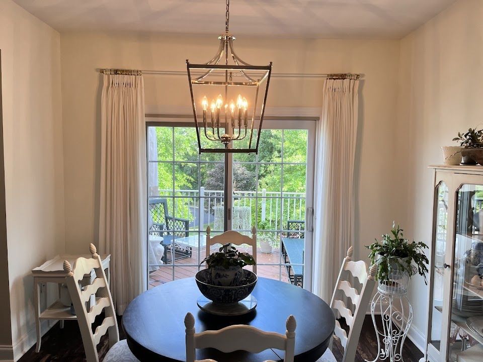 Dining room with round table, chairs, and light fixture over a sliding glass door with curtains.