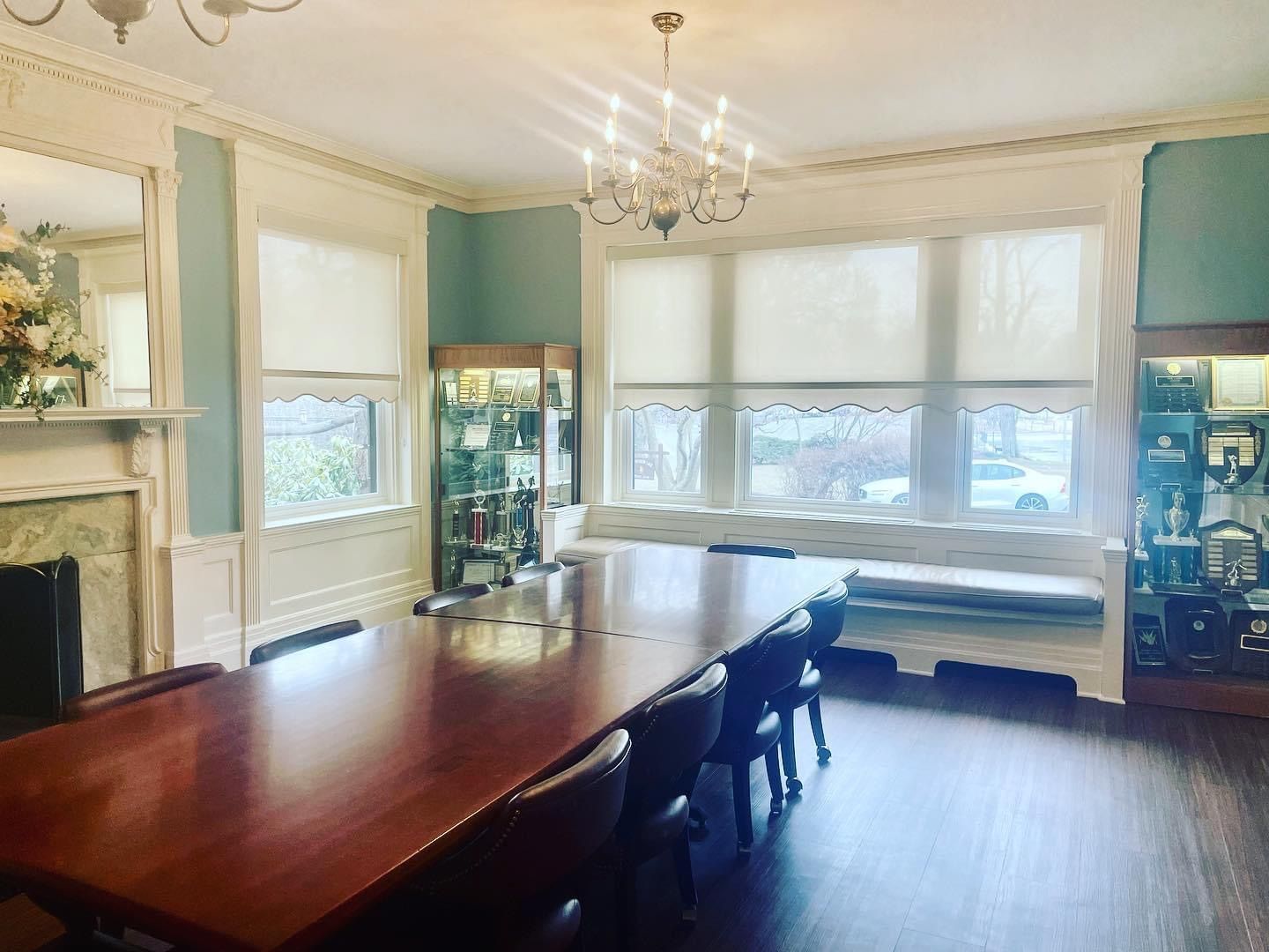 Formal dining room with long wooden table, chairs, and a chandelier. Built-in windows with shades, cabinets, and fireplace.