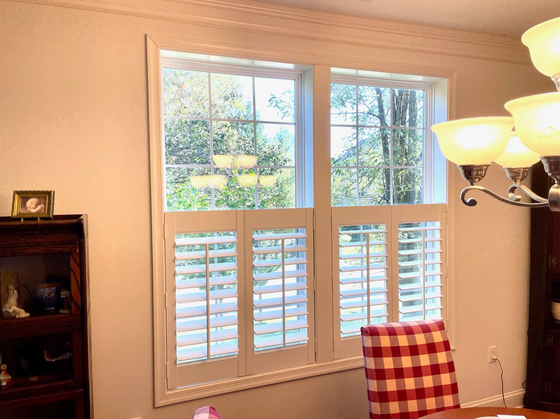 Window with white shutters, a checked chair, and a chandelier.