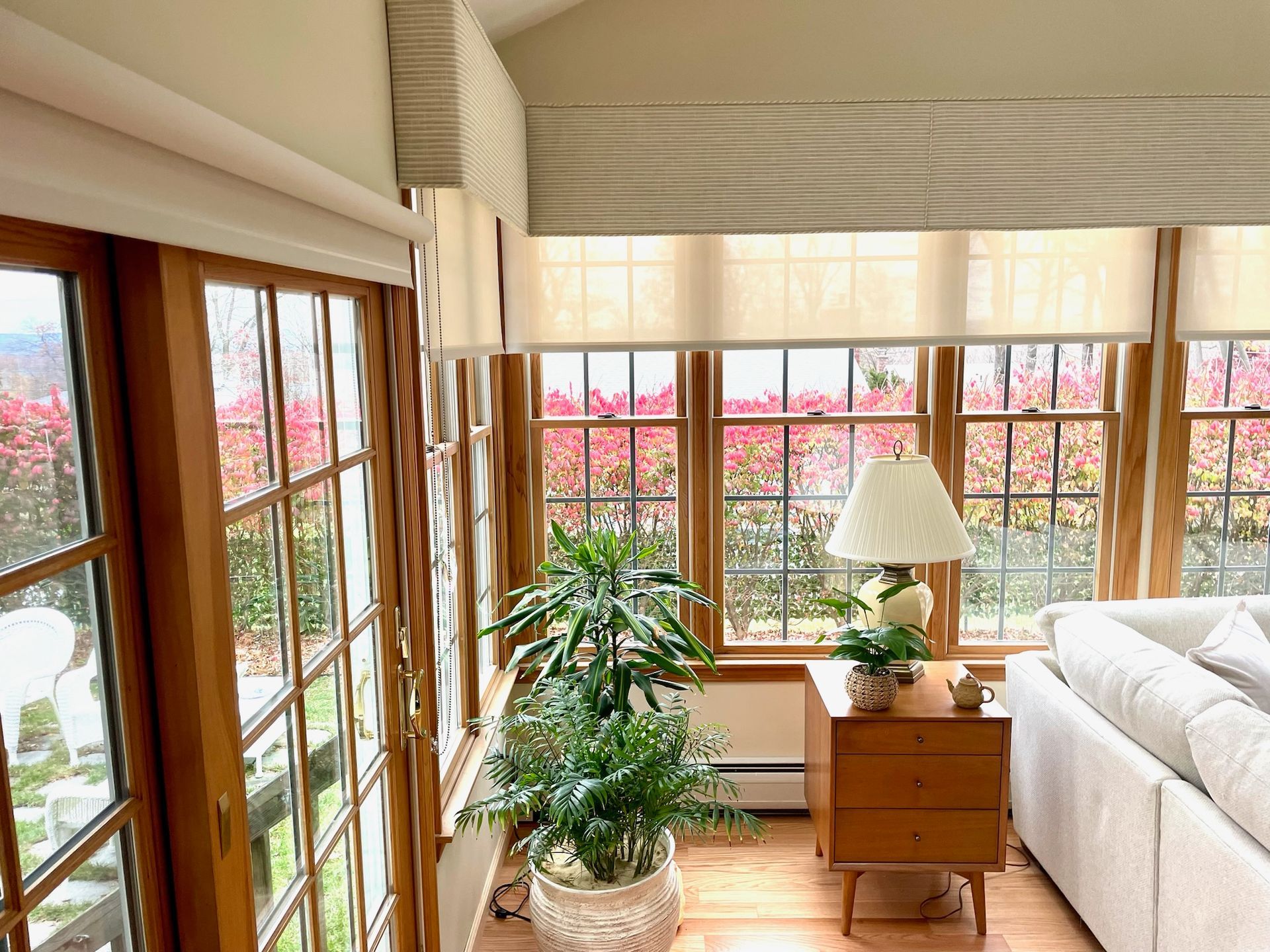 Sunroom with large windows, plants, and a sofa, looking out on foliage.