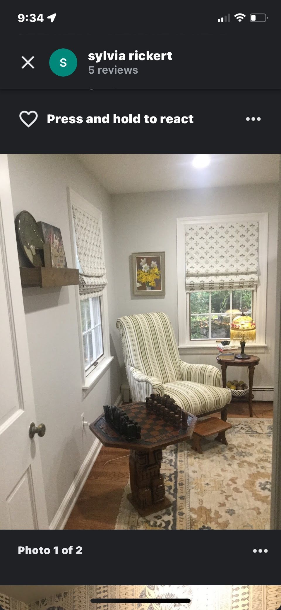 A room with a patterned armchair, a small table, and windows with patterned shades; neutral walls.