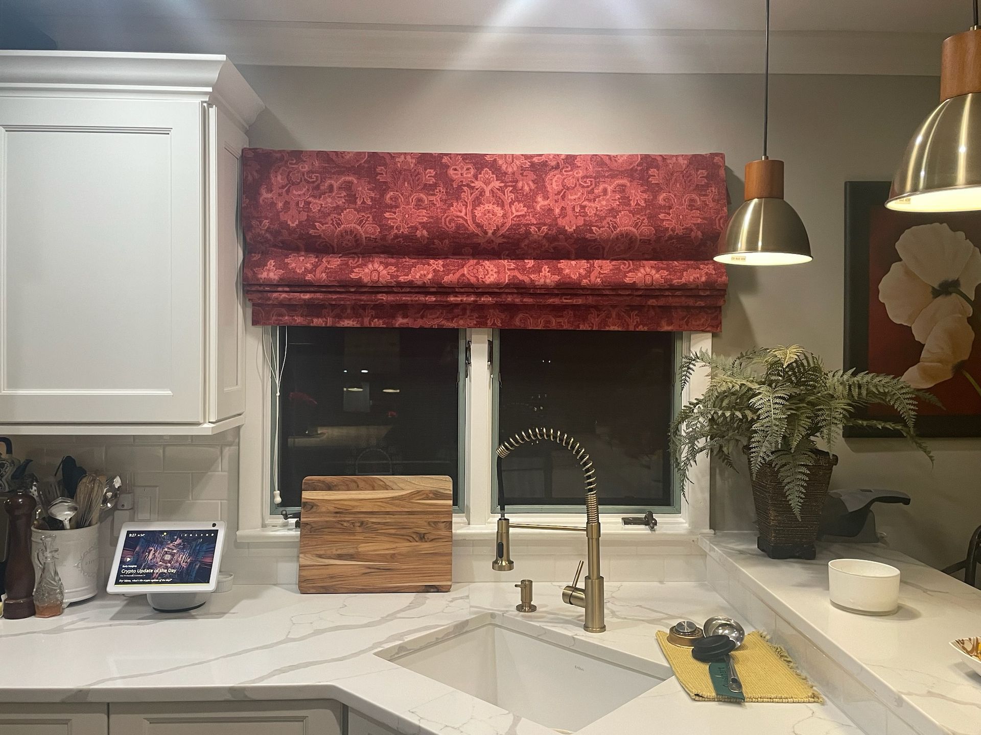 Kitchen with red patterned roman shade over the window, white cabinets, sink, and countertop.