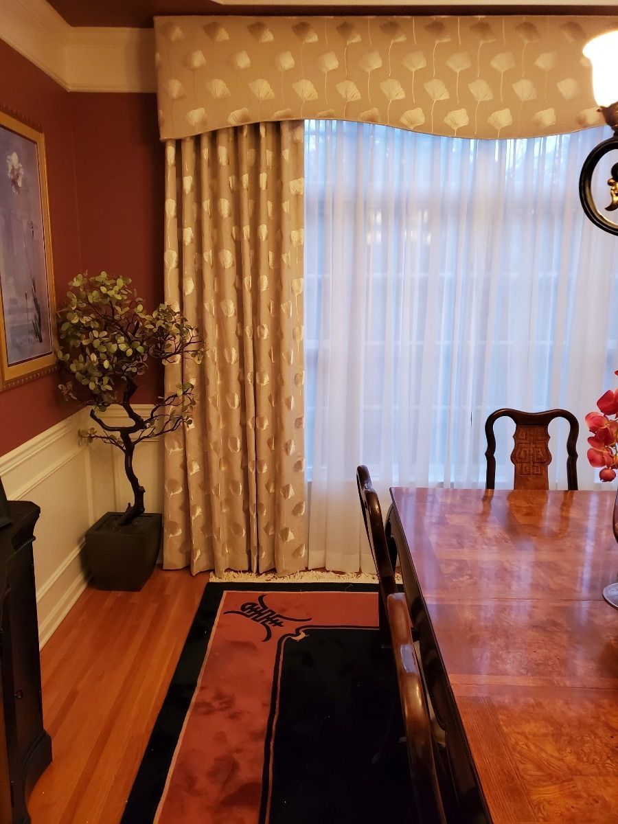 Formal dining room with draped window, long wood table, and red wall.