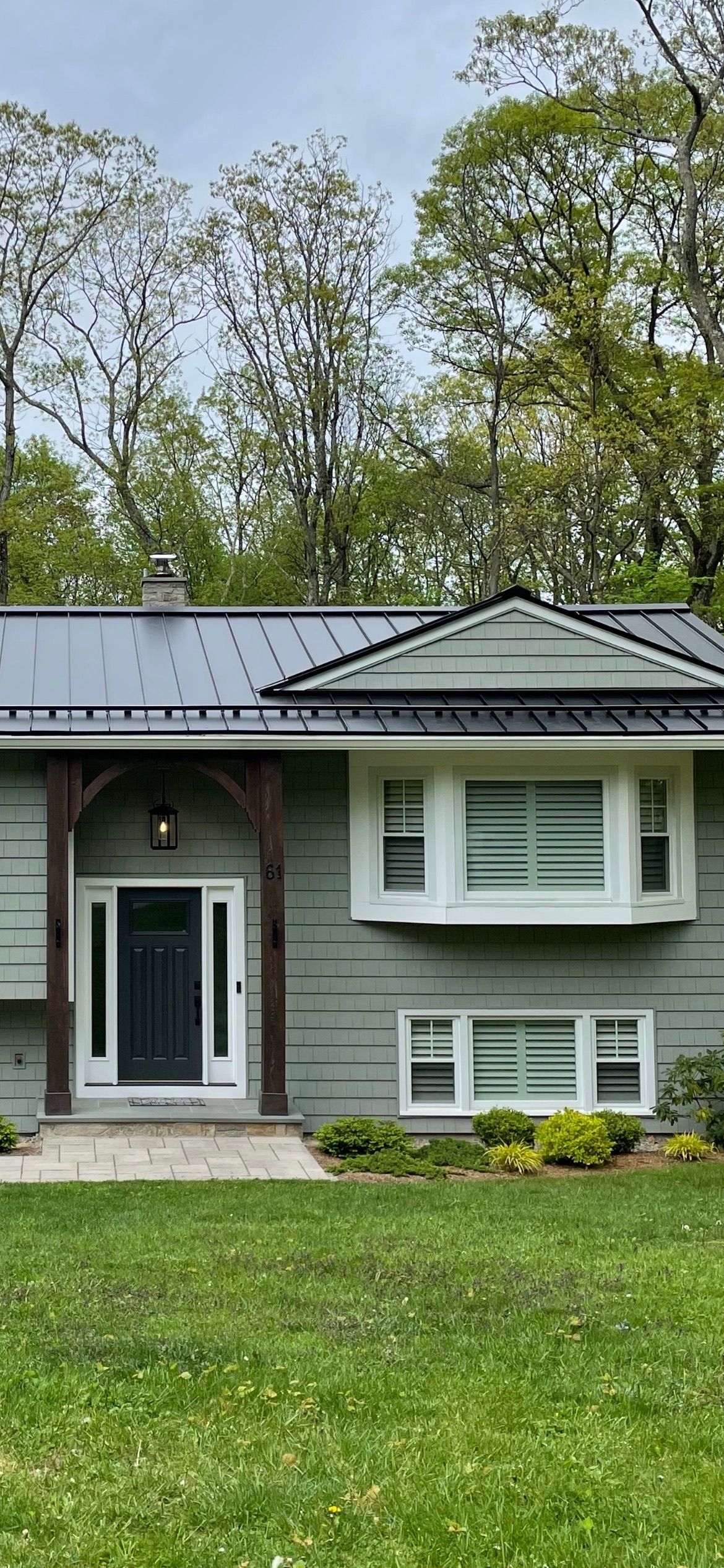 A green house with a dark door and black roof, set against a backdrop of trees and grass.
