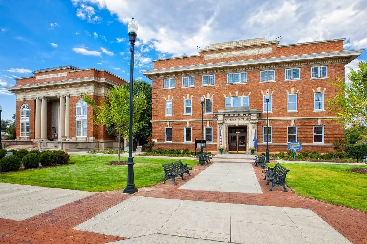 Brick academic building with white columns, lawn, walkway, and a second brick building under a blue sky