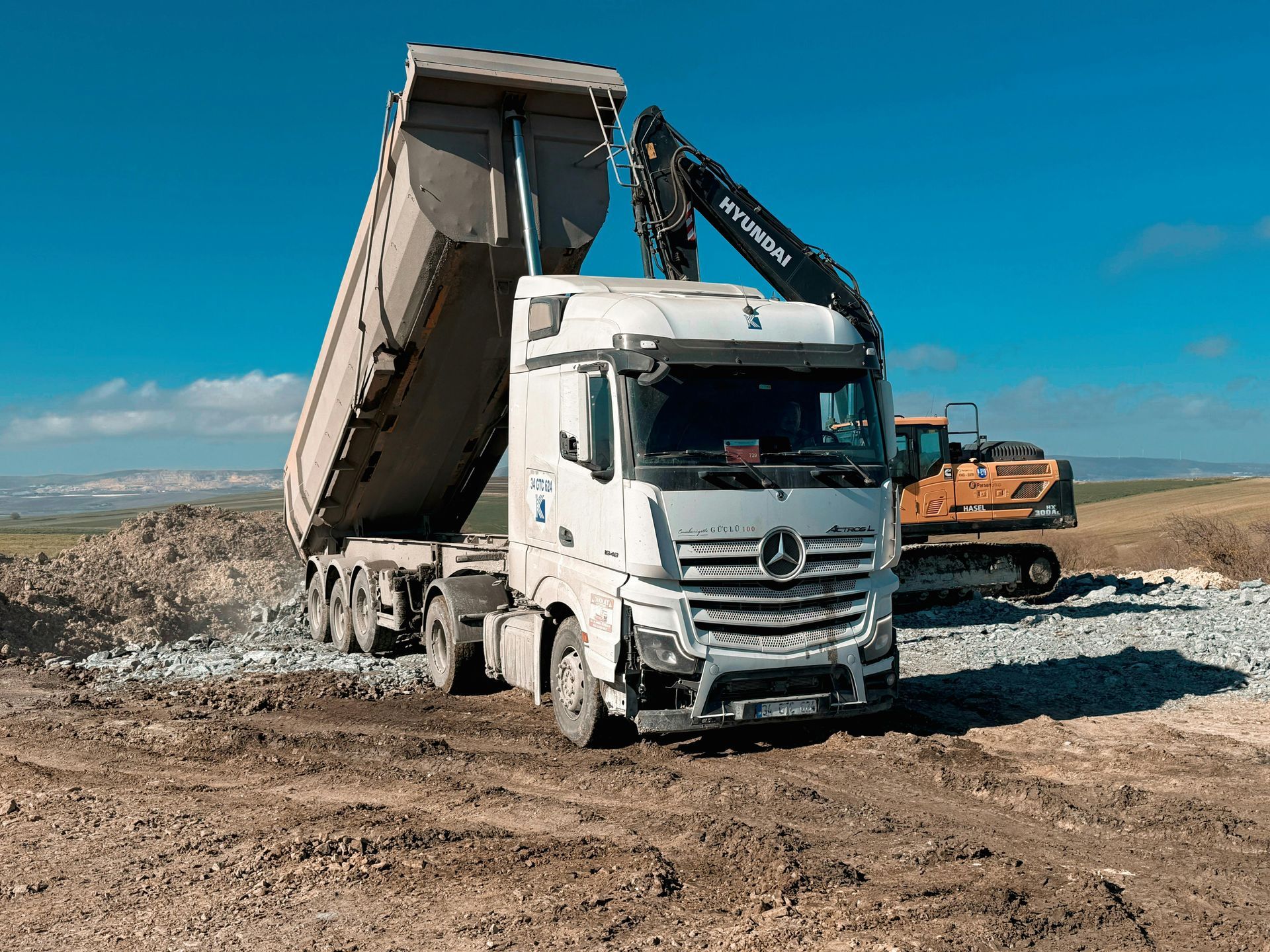 White dump truck unloading dirt at a construction site under a blue sky.