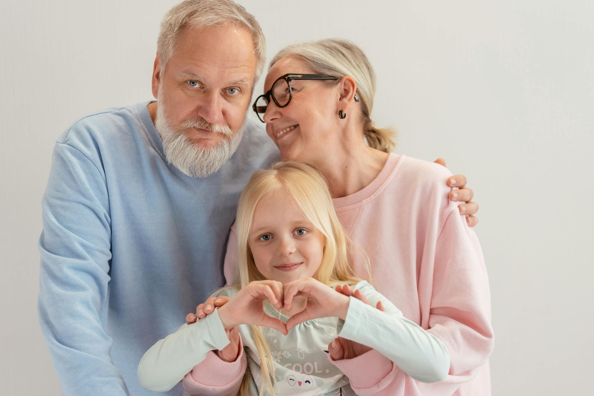 Three people posing together, with a child making a heart shape in front.