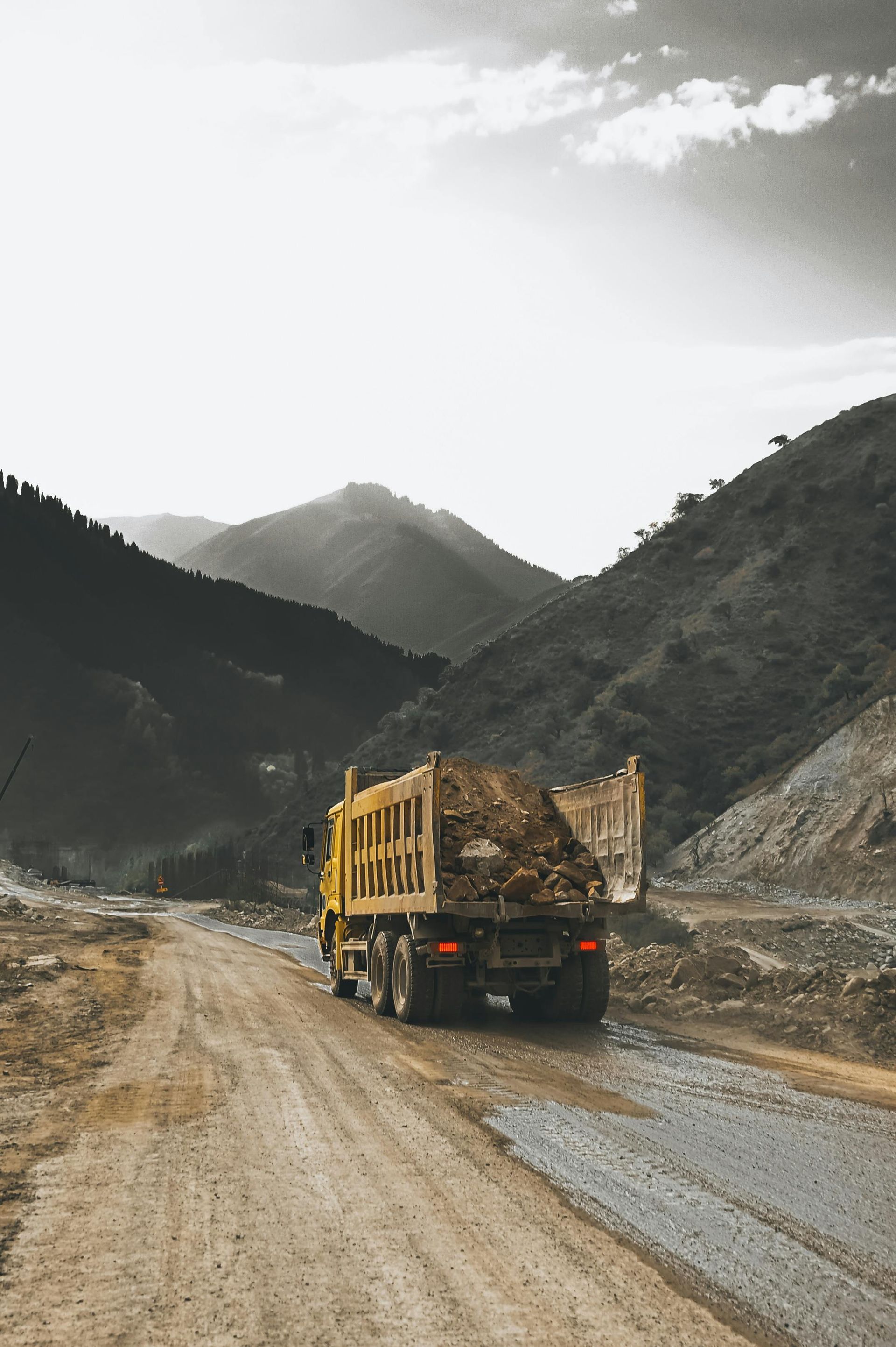 Truck loaded with logs driving on a muddy mountain road between steep hills