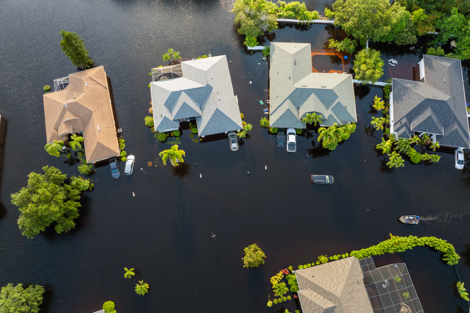 Aerial view of flooded suburban houses, with roofs and trees surrounded by dark water.
