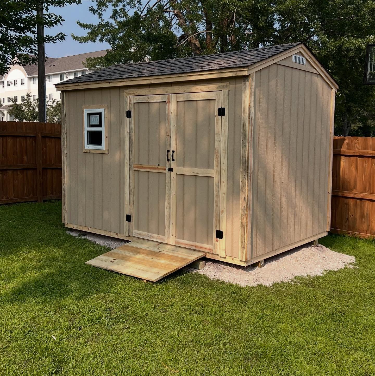 Wooden garden shed with double doors, small window, and ramp in a grassy backyard.