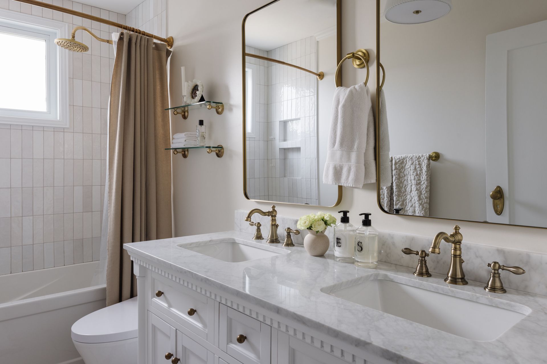 Bathroom with a double sink vanity, gold fixtures, marble countertop, and a white tiled shower.