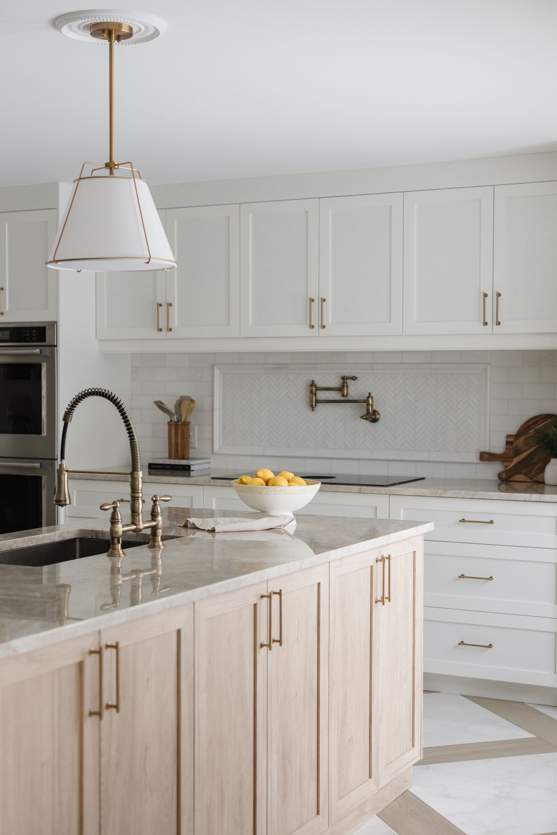Elegant kitchen with white cabinets, light wood island, gold hardware, and a hanging light.