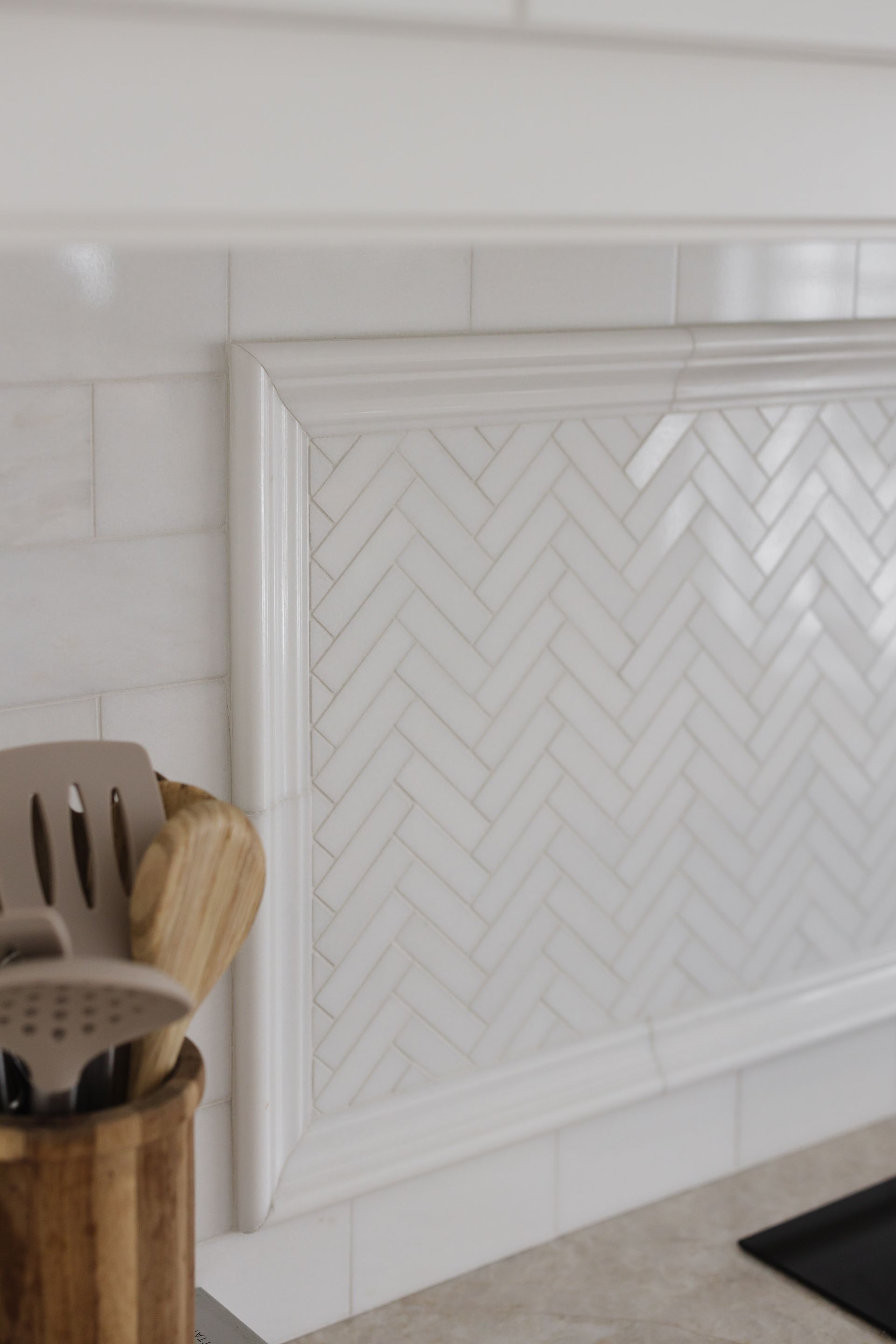 White tile backsplash with herringbone pattern, framed by molding in a kitchen.