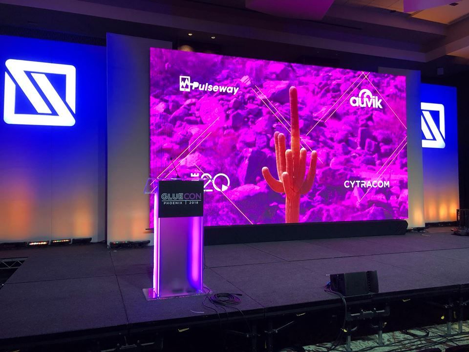 Custom conference stage design featuring an LED video wall, branded presentation graphics, and illuminated scenic elements