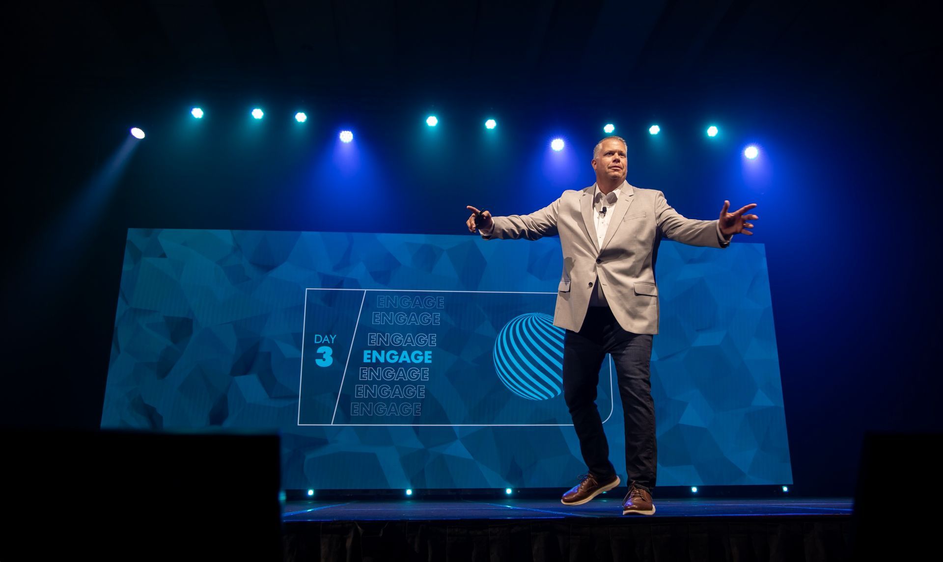 Keynote speaker presenting on stage with a large LED backdrop during a corporate conference.