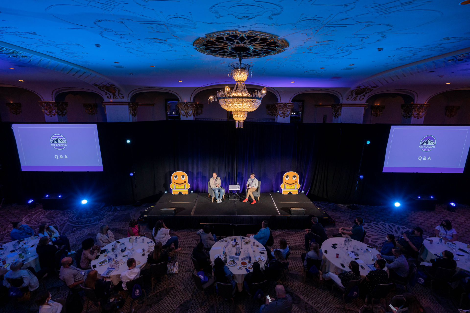 Panel discussion on a ballroom stage during a corporate conference with LED screens and audience seating.