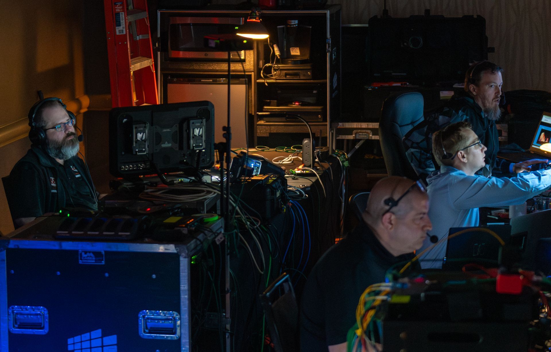 People working at computer stations in a dimly lit control room with monitors and cables