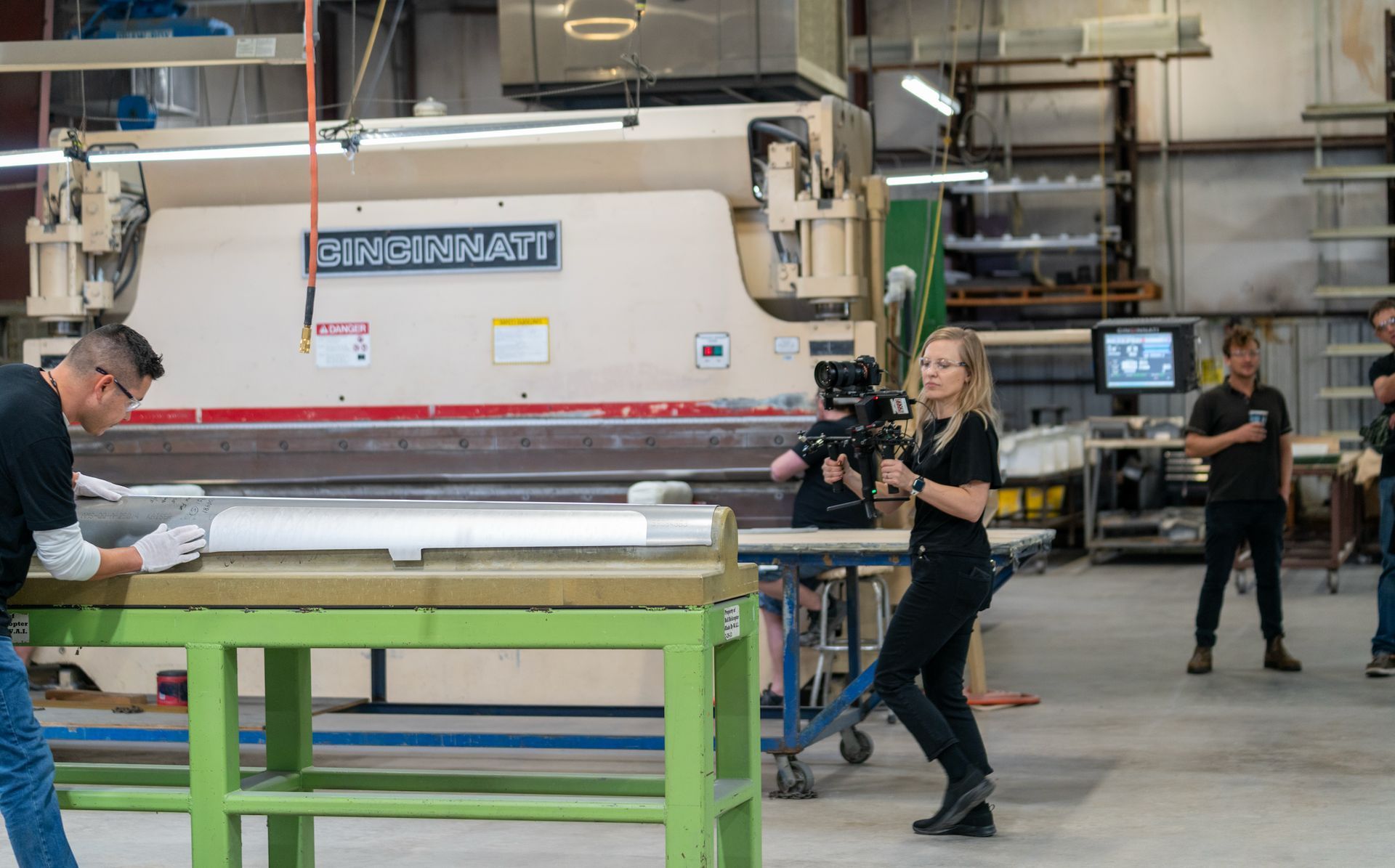 Camera operator filming industrial manufacturing operations for a corporate brand video.