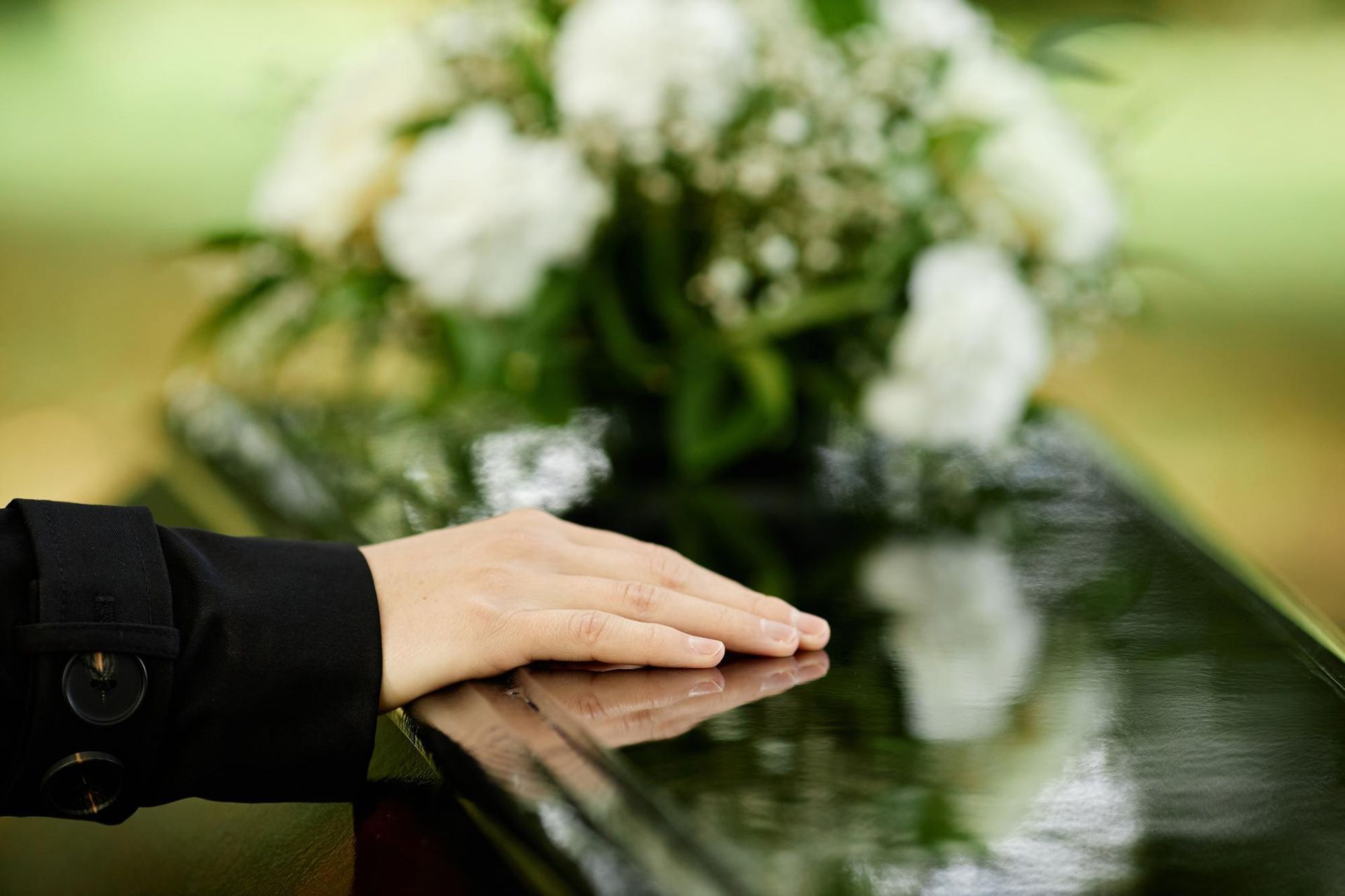A person is laying their hand on a coffin at a funeral.