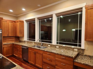 Empty kitchen with wooden cabinets, granite countertops, and a large window above the sink at night