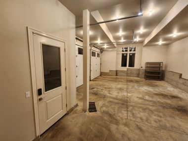 Empty unfinished room with beige walls, exposed ceiling lights, and bare concrete floor.
