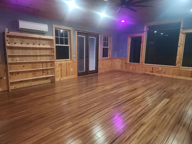 Empty wooden studio room with polished floor, windows, and purple ceiling lights