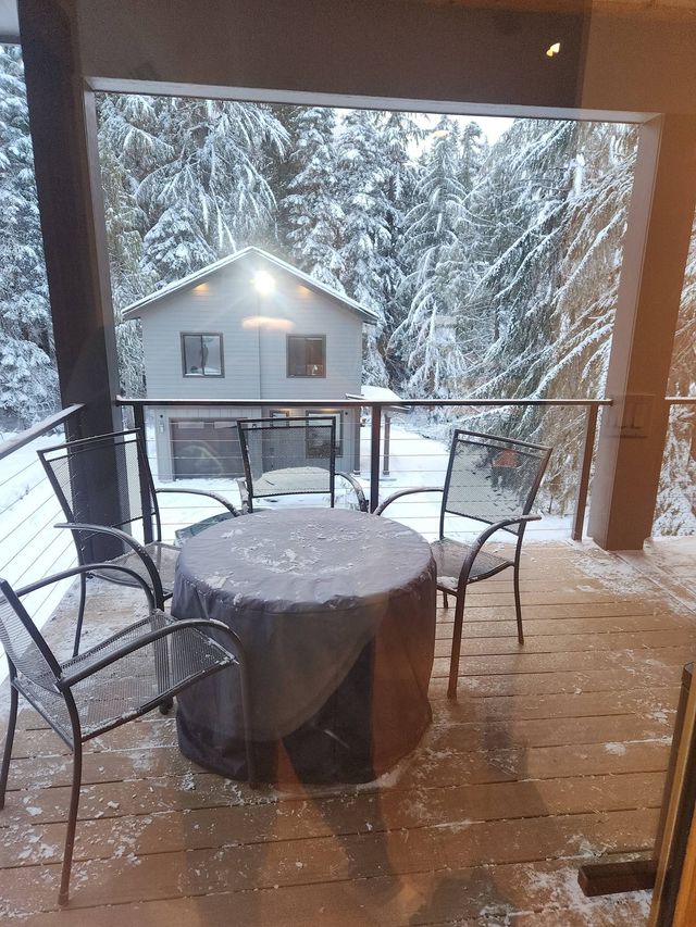Snowy porch with patio table and chairs overlooking a house in winter.