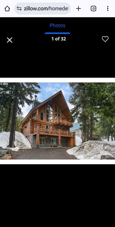 A rustic wooden chalet in a snowy forest, with tall pine trees and rocky ground.