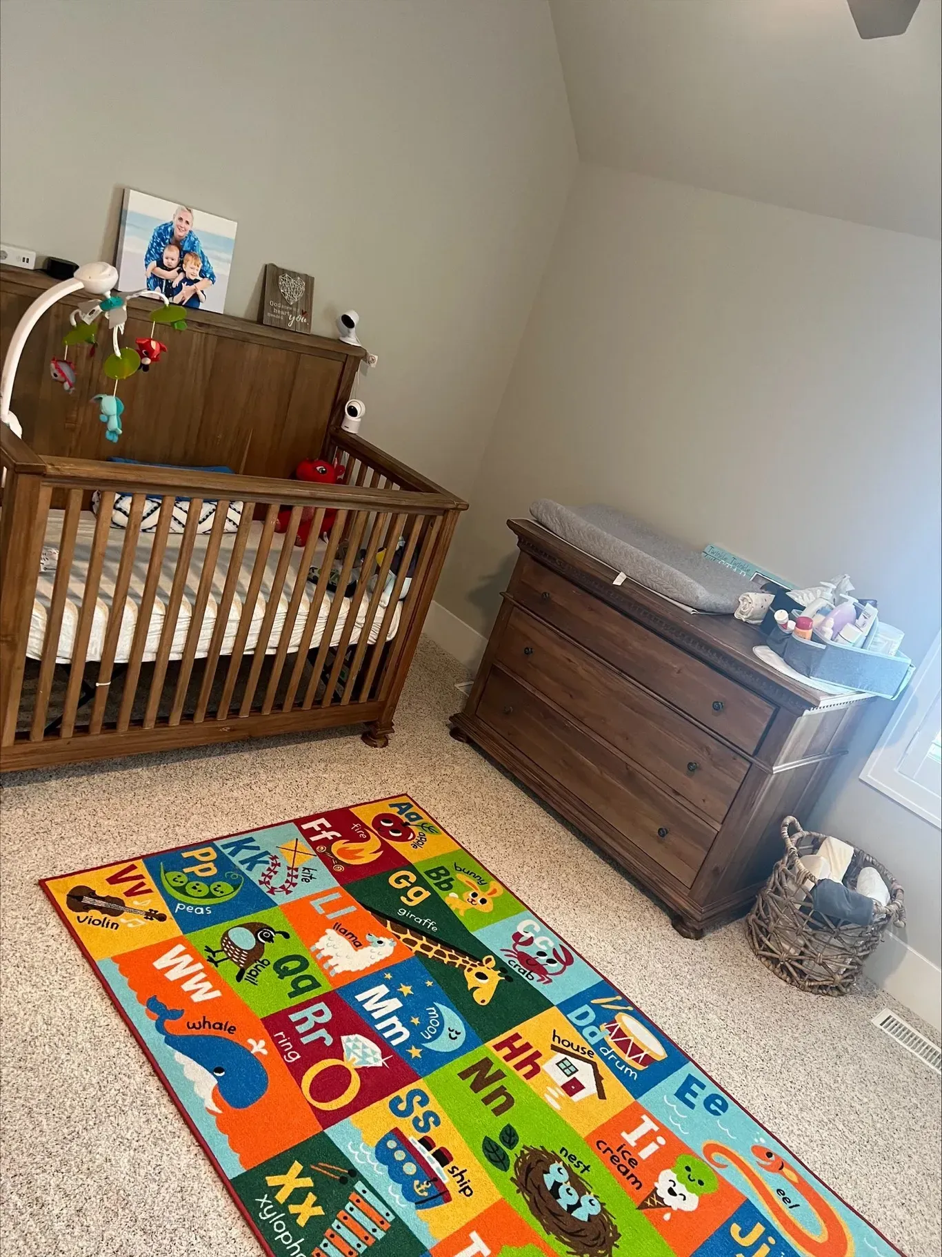 A nursery with a wooden crib, dresser, and colorful alphabet rug.