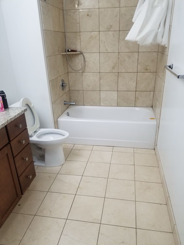 Bathroom with white toilet, bathtub, and tan tile floor and wall. Wooden vanity on the left.