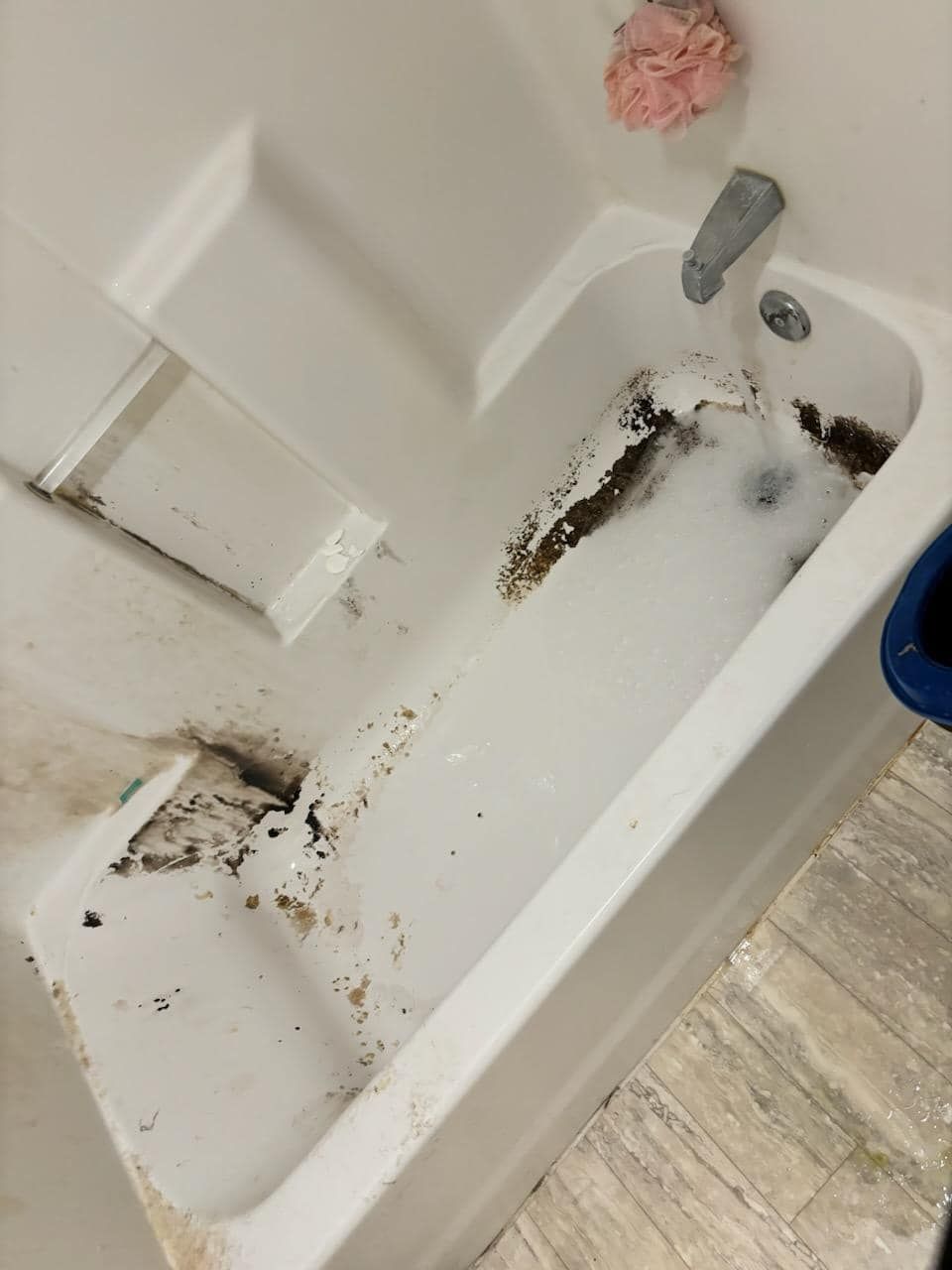 Dirty white bathtub with debris and soap scum.